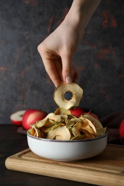 Elmalar ve kurutulmuş elmalar kasede ve kadın eli koyu arka planda.