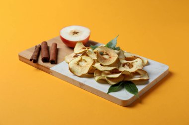 Elma dilimleri, tarçın çubukları ve sarı arka planda yarım elma.