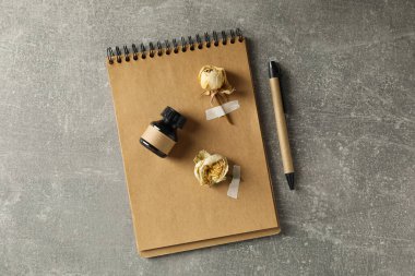 Kurumuş gül tomurcukları, not defteri ve gri arka planda bir şişe mürekkep.