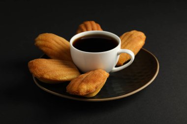 Madeleine kekleri ve siyah arka planda bir fincan kahve, kapatın.