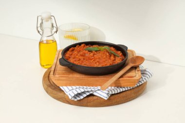 Kızartma tavasında bolonez sosu, tahta tahtalar, bir bardak su ve arka planda bir şişe yağ.