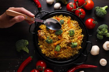 Kızartma tavasında pilav, sebzeler ve koyu ahşap arka planda kaşıkla el, üst manzara