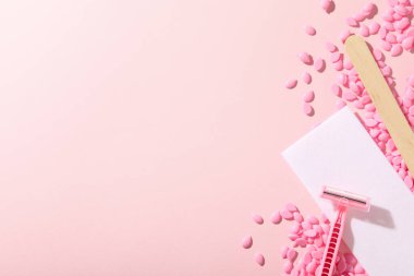 Tüy dökümü için balmumu tanecikleri ve pembe arka planda bir tıraş bıçağı.