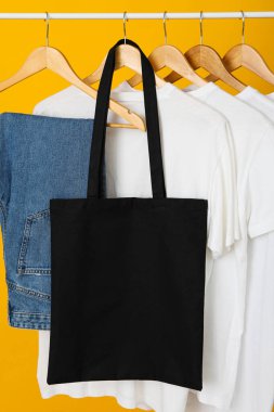 A black bag hangs on a hanger with clothes