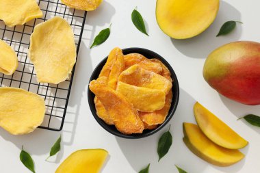 Bir kase kurutulmuş mango cipsi ve taze kesilmiş mango.