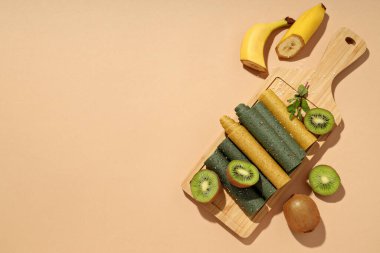 Tahta üzerinde meyve pastilleri, bej arka planda muz ve kivi yarıları, metin için boşluk