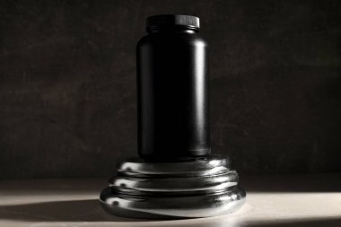 Siyah plastik kavanoz metal spor ekipmanları üzerinde koyu gri arka planda, yakın çekim