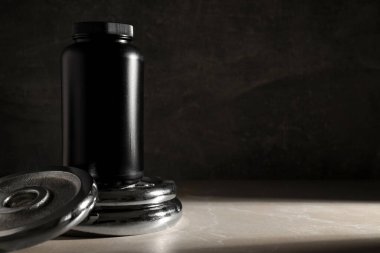 Koyu gri arka planda metal spor ekipmanları üzerinde siyah plastik kavanoz, metin için boşluk