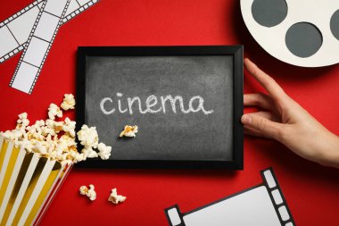 Tahta, kağıt bardakta patlamış mısır, film malzemeleri ve kırmızı arka plan, üst manzara.