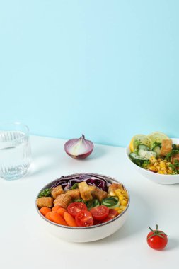 Beyaz bir masada taze sebzeli kızarmış tofu salatası.