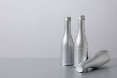 Gri arka planda üç gümüş cam şişe, mesaj için boşluk