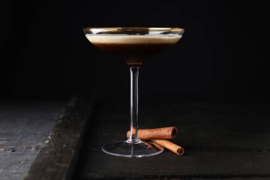 Bardakta martini espresso kokteyli ve koyu arkaplanda tarçın çubukları.