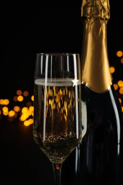 Siyah arka planda şampanya şişesi olan bir bardak.