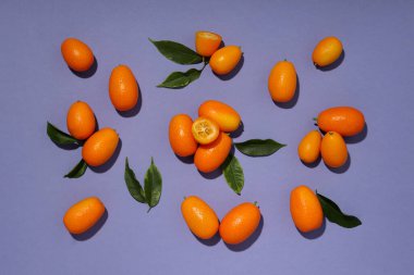 Tam ve kesim kumkat meyve ve yapraklar mor arka plan, üst görünüm