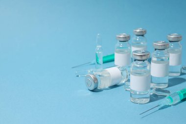 Mavi arka planda aşı ve şırıngalarla dolu cam tıbbi şişeler ve ampuller.