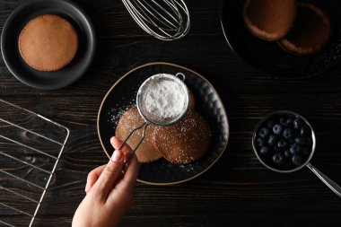Tabaklarda çikolatalı gözleme, böğürtlen, şeker tozu ve ahşap arka planda el.