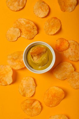 Sarı arka planda hardallı patates cipsi.
