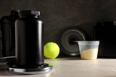 Siyah plastik kavanozlar ve şişe, ölçü kabı ve spor ekipmanları koyu gri arka planda, metin için boşluk