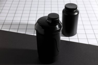 Siyah plastik kavanoz ve siyah beyaz arka planda şişe, kapatın.