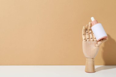Mankenin ahşap elinde kozmetik bir şişe.