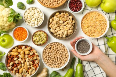 Kâselerde vegan protein ürünleri seti ve beyaz arka planda el, üst görünüm