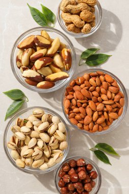 Beyaz arka planda şeffaf cam kaselerde farklı tipte fındıklar.