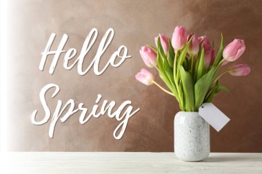 Merhaba bahar, pembe laleler bir vazoda kahverengi bir zemin üzerinde