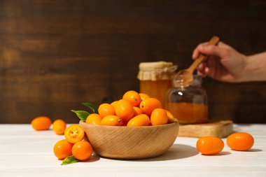 Kumkuat kasede, reçel kavanozu ve kaşık elinde ahşap arka planda duruyor.
