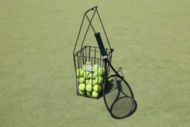 Yeşil arka planda bir sepet topla tenis raketi..