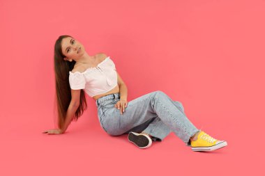 Çekici bir genç kız pembe bir arka planda oturuyor.