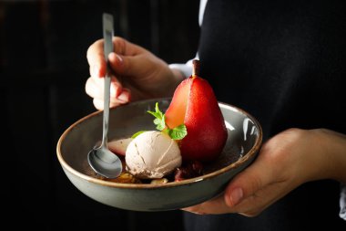 Dondurma ve armut şarapta tabakta ve kaşık ellerde koyu arka planda