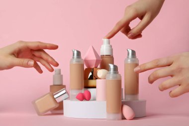 Vakıf şişeleri, kadın elleri, kozmetik fırçası ve pembe arka planda süngerler.