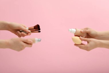 Vakıf şişeleri, kozmetik süngerler ve pembe arka planda kadın ellerinde fırçalar.