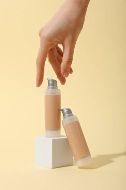 Bej arka planda fondöten şişeleri ve kadın eli