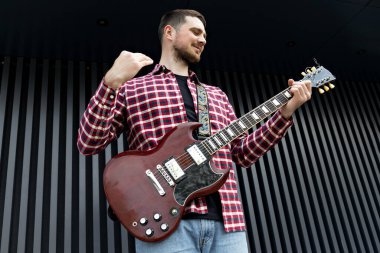 Kaliteli bir genç adam koyu bir arka planda gitar çalar.