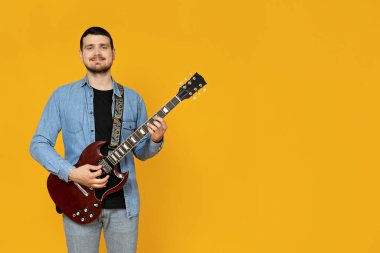 Elinde sarı bir arka planda gitar olan çekici bir genç.