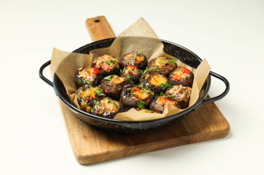 Kızartma tavasına doldurulmuş mantarlar ve beyaz arka planda mutfak tahtası.