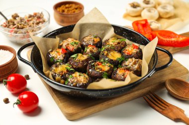 Kızartma tavasına doldurulmuş mantar, mutfak tahtası ve malzemeler beyaz arka planda, kapat.