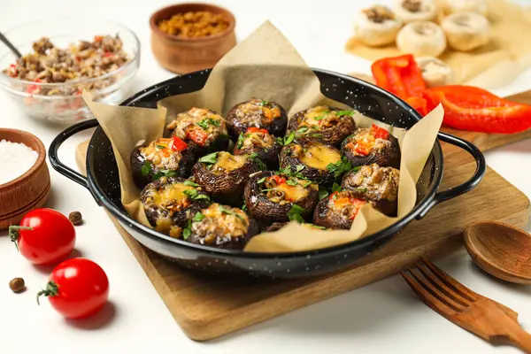 Kızartma tavasına doldurulmuş mantar, mutfak tahtası ve malzemeler beyaz arka planda, kapat.