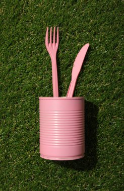 Yeşil arka planda pembe teneke kutu ve plastik çatal bıçaklar.