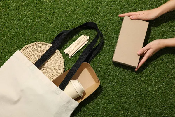 Pamuk torba ve kutu ellerinde yeşil arka plan, üst görünüm
