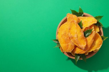 Yeşil arka planda bir kasede kurutulmuş mango cipsi.