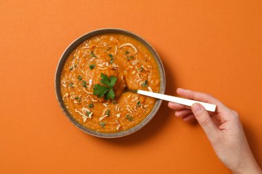 Tatlı patates püresi kasede ve kaşık elinde turuncu arka planda, üst manzara