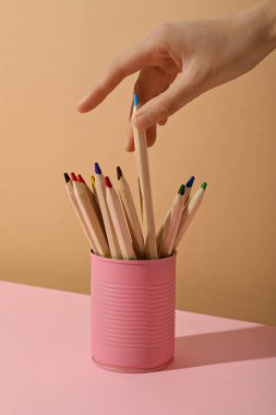 Renkli kalemler pembe teneke kutuda ve bej arka planda.