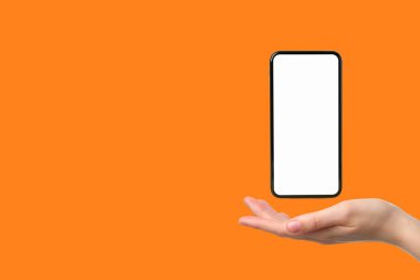 El, turuncu arka planda boş ekranı olan minimalist bir akıllı telefonu tutuyor.