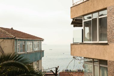 Binalar, uzakta tekneleri olan sakin bir okyanusa bakar.