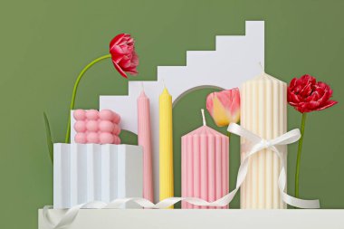 Parlak renkli mumlar ve çiçekler bir rafta canlı bir görüntü oluşturur.