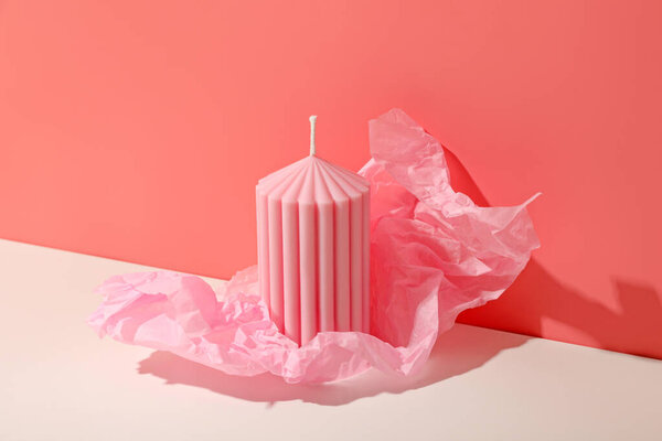 Soft pink candle placed on a surface with crumpled tissue nearby