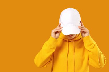 Parlak sarı kapüşonlu bir kapüşonlu giyerken beyaz şapkayı ayarlayan kişi