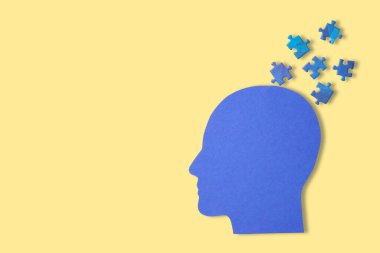 Sarı arkaplanda bulmaca parçaları olan mavi baş silueti